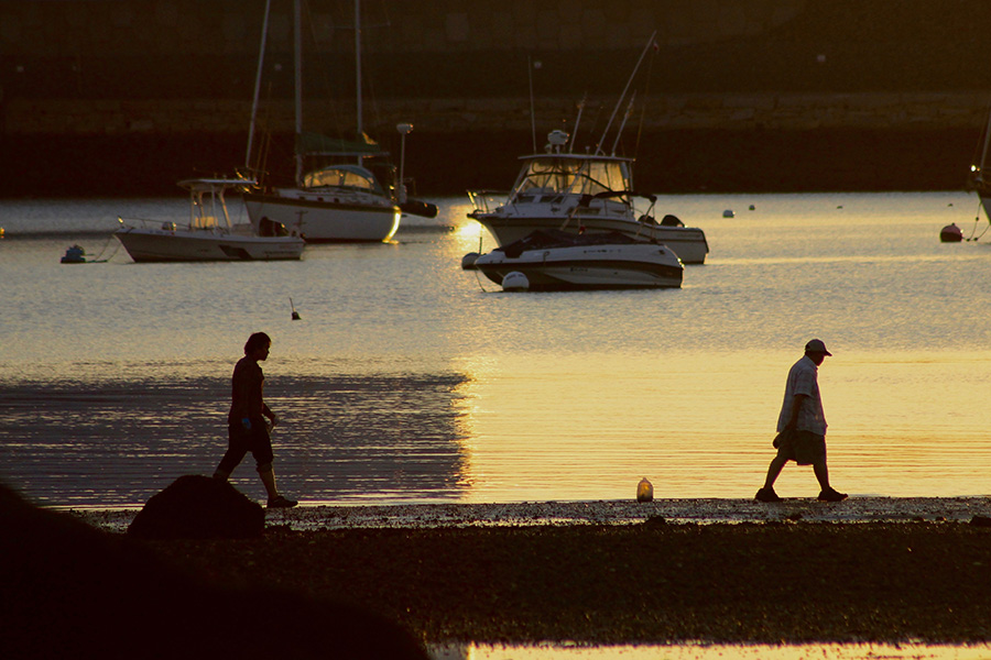 Color photograph: Harbor in low, yellow light, figures in silhouette