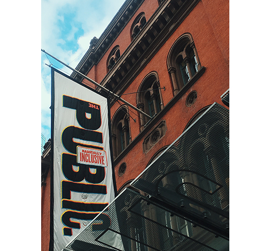 Photograph of the facade of The Public Theater in Manhattan, a banner that says "THE PUBLIC" and "RADICALLY INCLUSIVE" on prominent display.