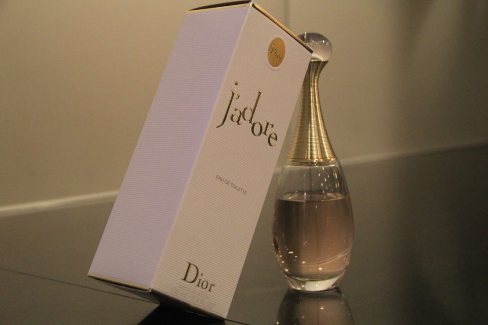 A perfume bottle with light pink liquid sits on a table, its box leaning against it. 