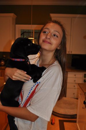 A young woman hugs a small black dog, looking away from the camera. 