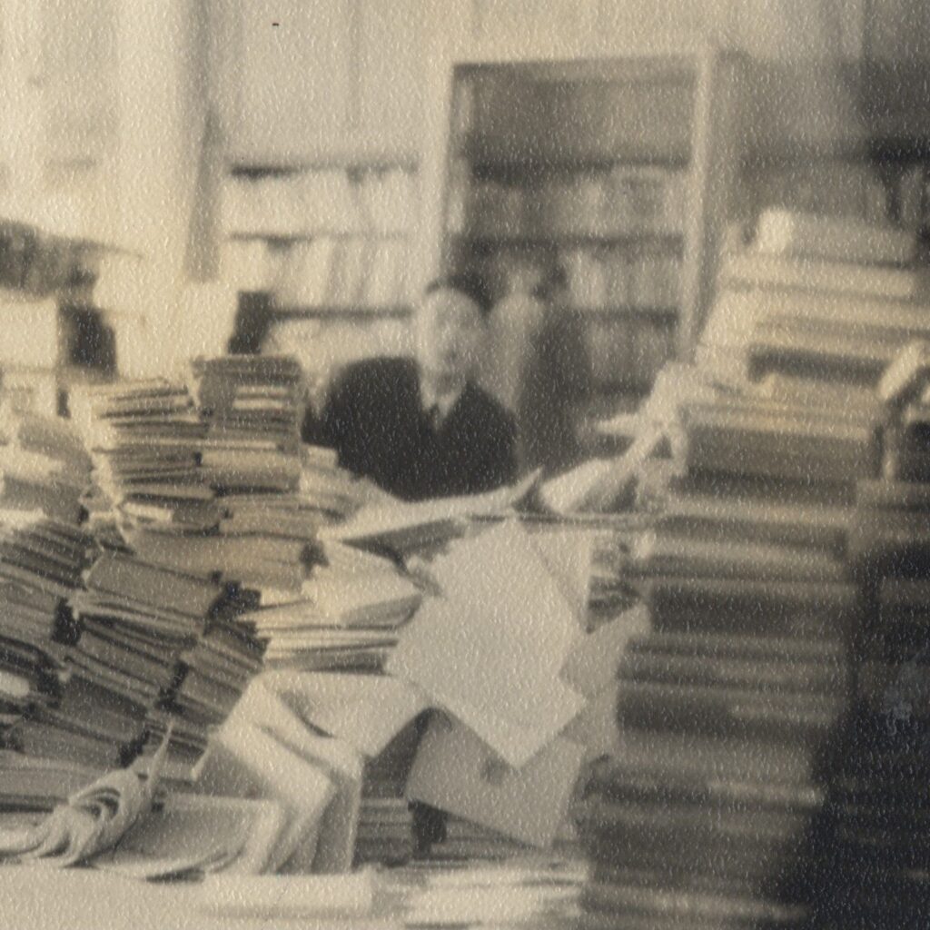 A librarian sits amid piles of books and papers.