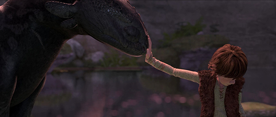 a boy extends his harm to touch the snout of a dragon (animated still)