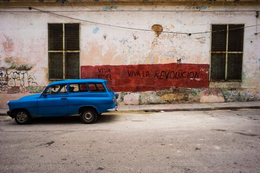 Blue car in front of a building on which "viva fidel" and "viva la revolucion" are painted