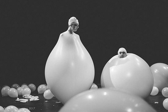 Two people whose bodies are white balloons, surrounded by white balloons on the floor. 