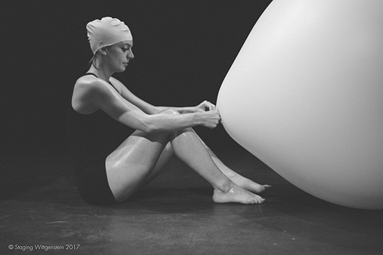 A woman with a balloon on her head seated facing a large white balloon.