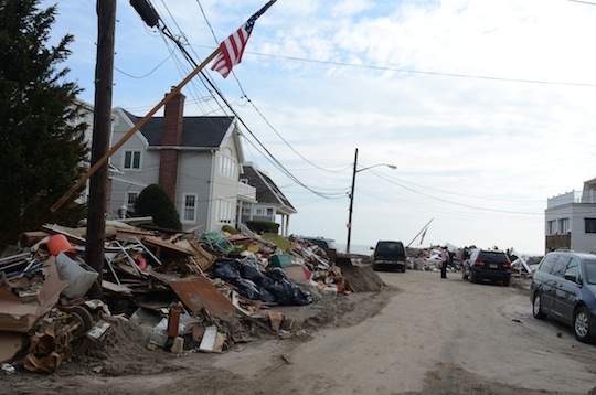 A neighborhood street with an American flag flying; wreckage lining the curb. 