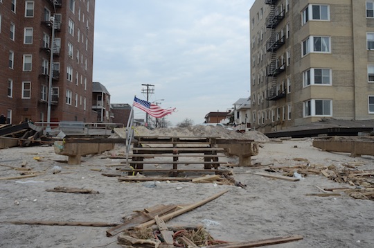 Devastation in an empty lot; a tattered American flag flying. 