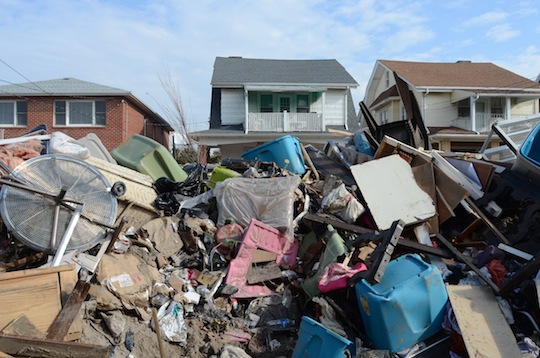 A view of a pile of wreckage, covering the houses behind it. 