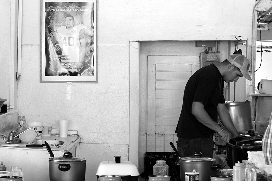 A man working in a full kitchen of pots and pans with a football player's poster on the wall (in black and white). 