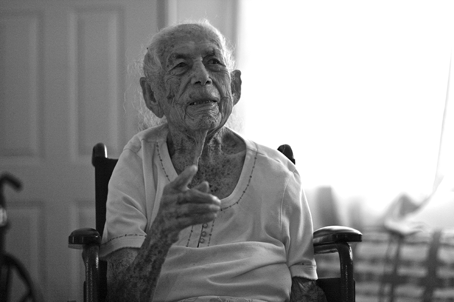 A portrait of an older woman in a chair, gazing off camera (in black and white). 