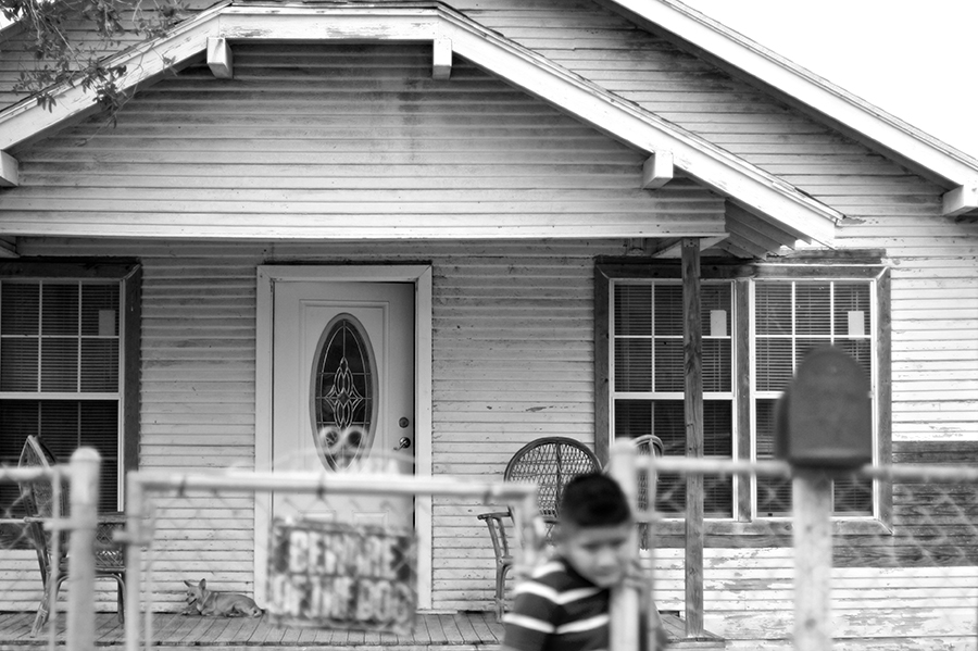 The front porch of an older home, with a young boy exiting the fence and a "beware of dog" sign.