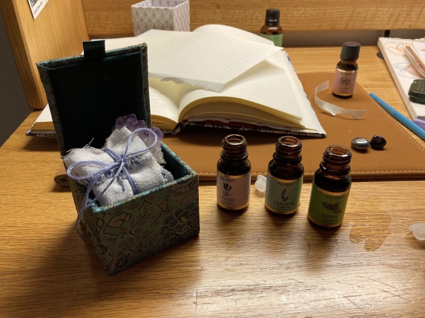 A notebook, a small box holding a piece of cloth with a bow, and some bottles of essential oils sit on a table.