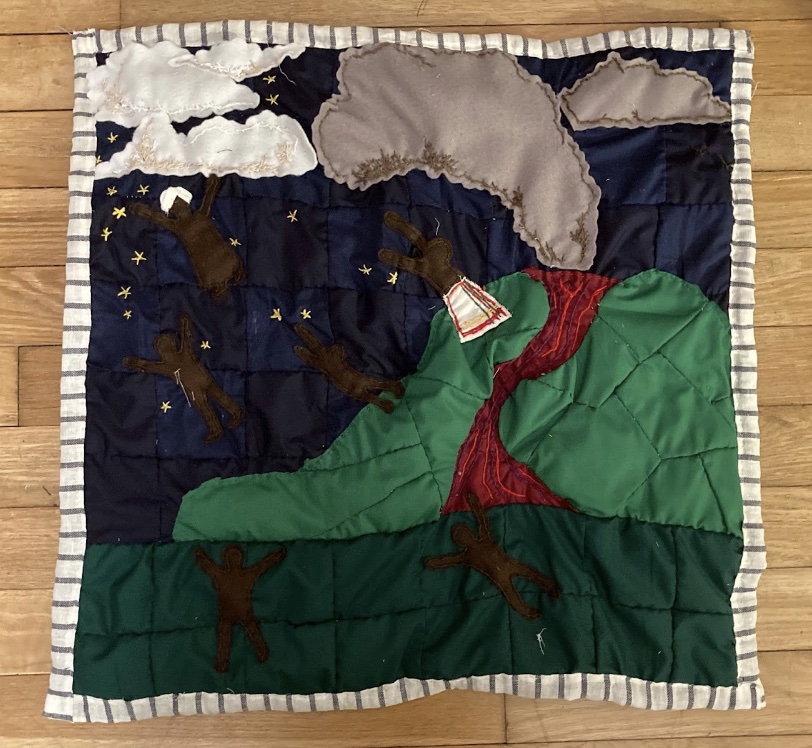 An overhead view of the volcano quilt: a landscape of a dark blue sky, dark green ground, and a light green erupting volcano and white clouds is adorned with dark figures—representing the enslaved—flying.