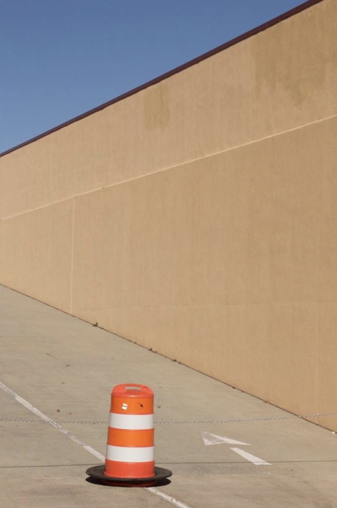 concrete road and concrete wall with orange construction cone and arrow in foreground