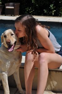 A girl kisses her dog, sitting on the edge of a pool.