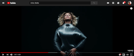 A screengrab of the music video shows Beyonce against a black background in blond cropped hair covering her face with her body covered in shiny blue cloth that she presses to her body.