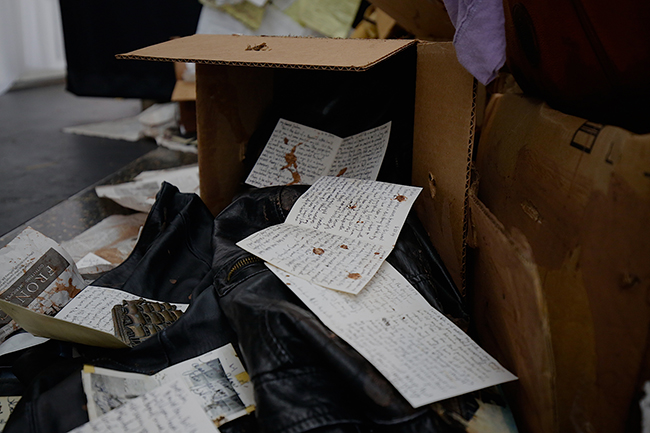 A cardboard box turned over, spilled contents include pages of handwritten papers and a leather jacket. 