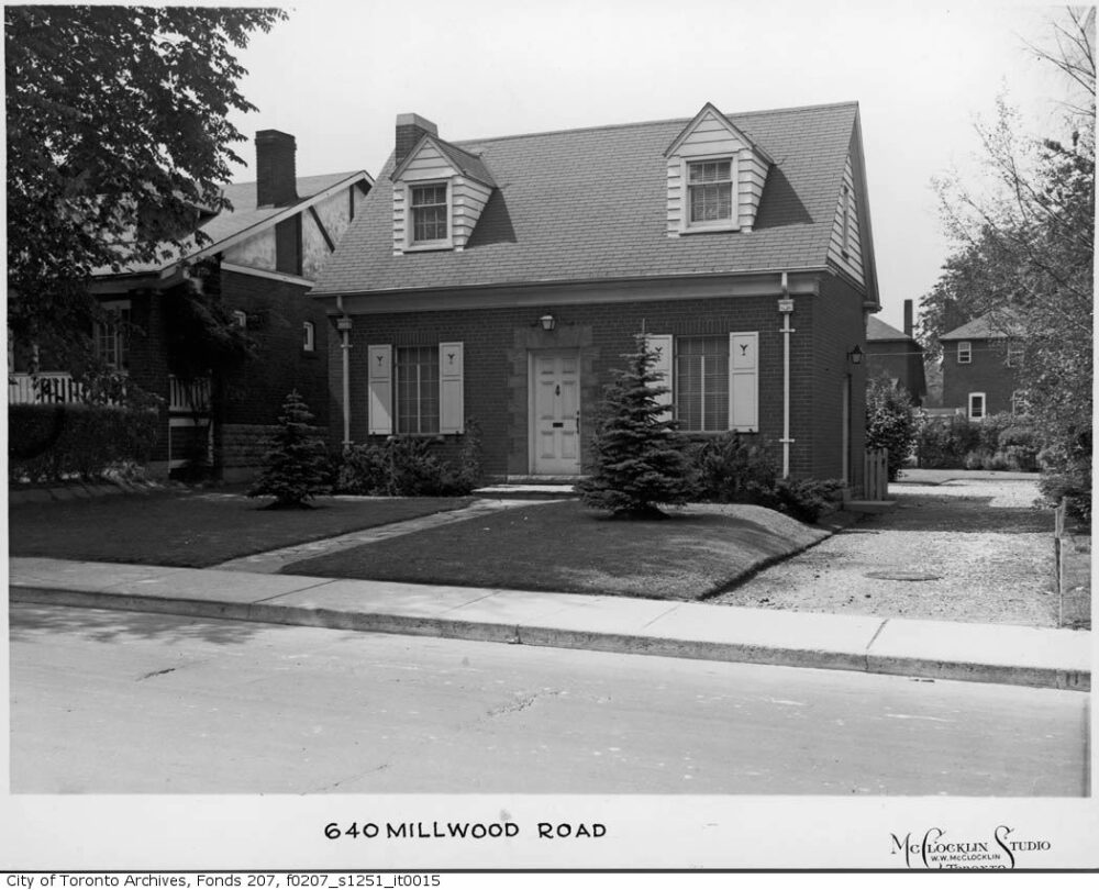 A black and white photograph of hydro substation that looks like a suburban home with a tree on the lawn