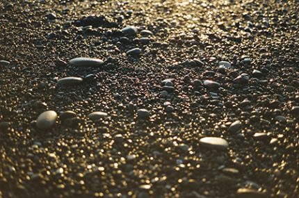 small rocks and sand on a pebble beach, hit with golden light