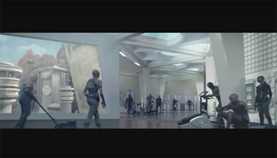 People walk and exercise using gym equipment in a windowed, white-walled, futuristic corridor
