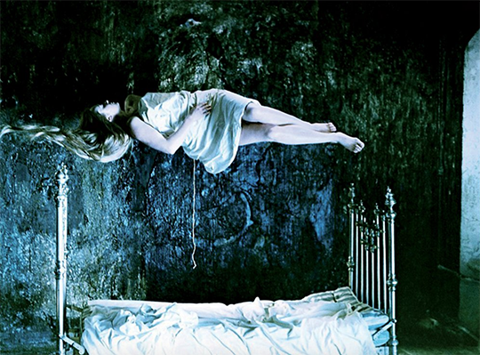 Woman in white nightdress, supine, levitating above a bed.
