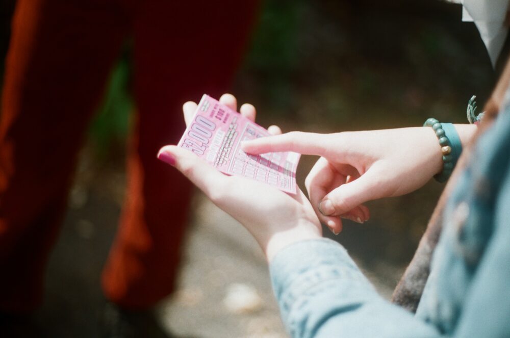 Hands holding a pink scratcher lotto ticket, pointing to a symbol.