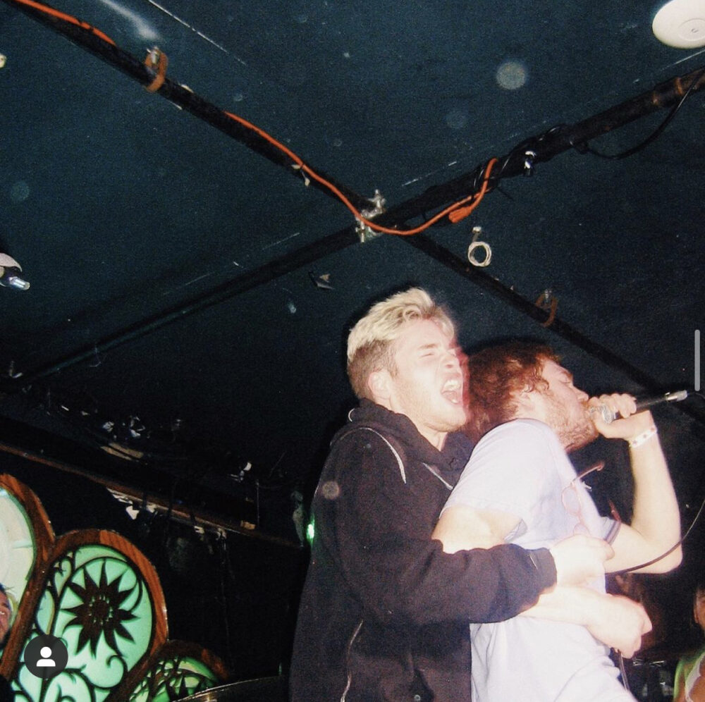 pictured Iz, in a black hoodie, emphatically embracing Jamie, wearing a white tee-shirt, as he performs during a Manwolves set.