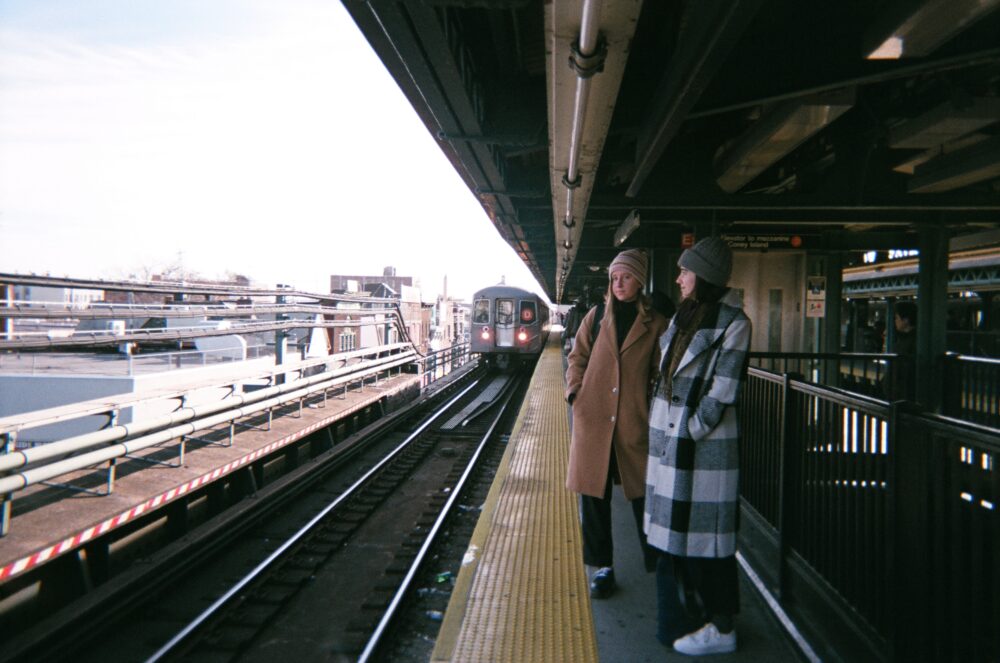 Lucy and Taylor, wrapped in winter coats and hats, wait for the D train at Bay Parkway station.