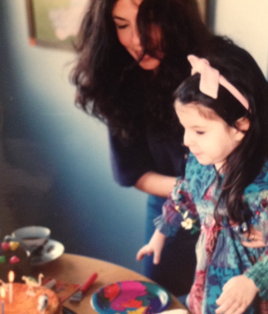 A young girl and her mother at a table with a birthday cake. 