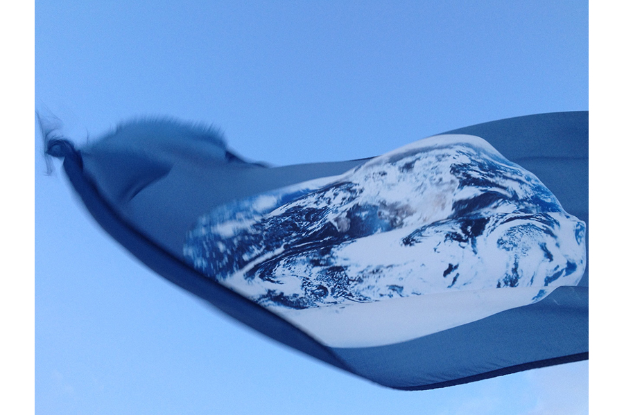Close-up of an Earth flag flying in the wind, the sky around it. 
