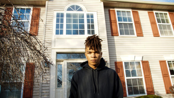 A photograph of the author wearing a black sweatshirt in front of his suburban childhood home