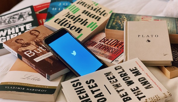 Photo of an iPhone displaying the Twitter load screen and set atop a stack of books.