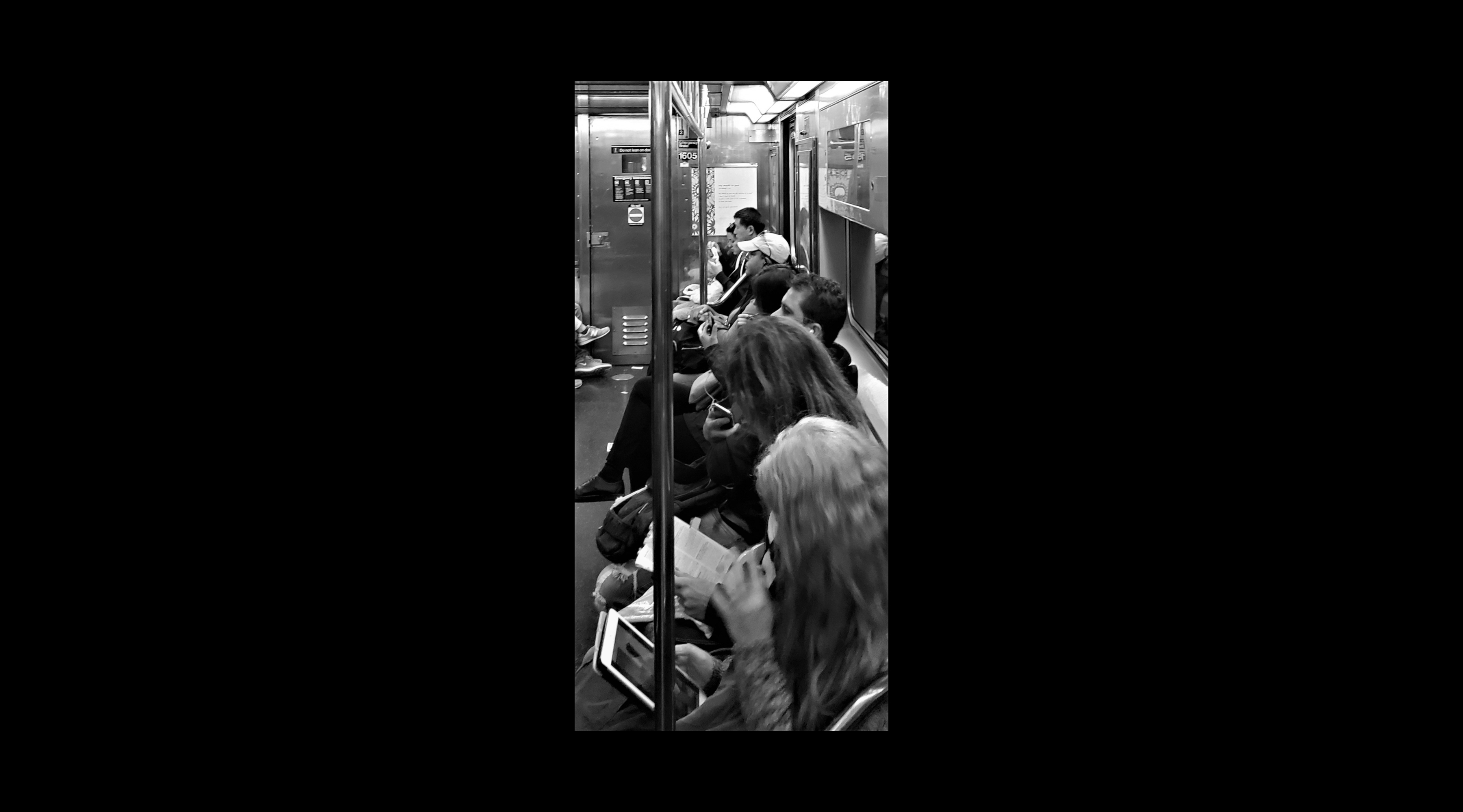 A row of subway commuters, from an angle slightly above their heads (in black and white)