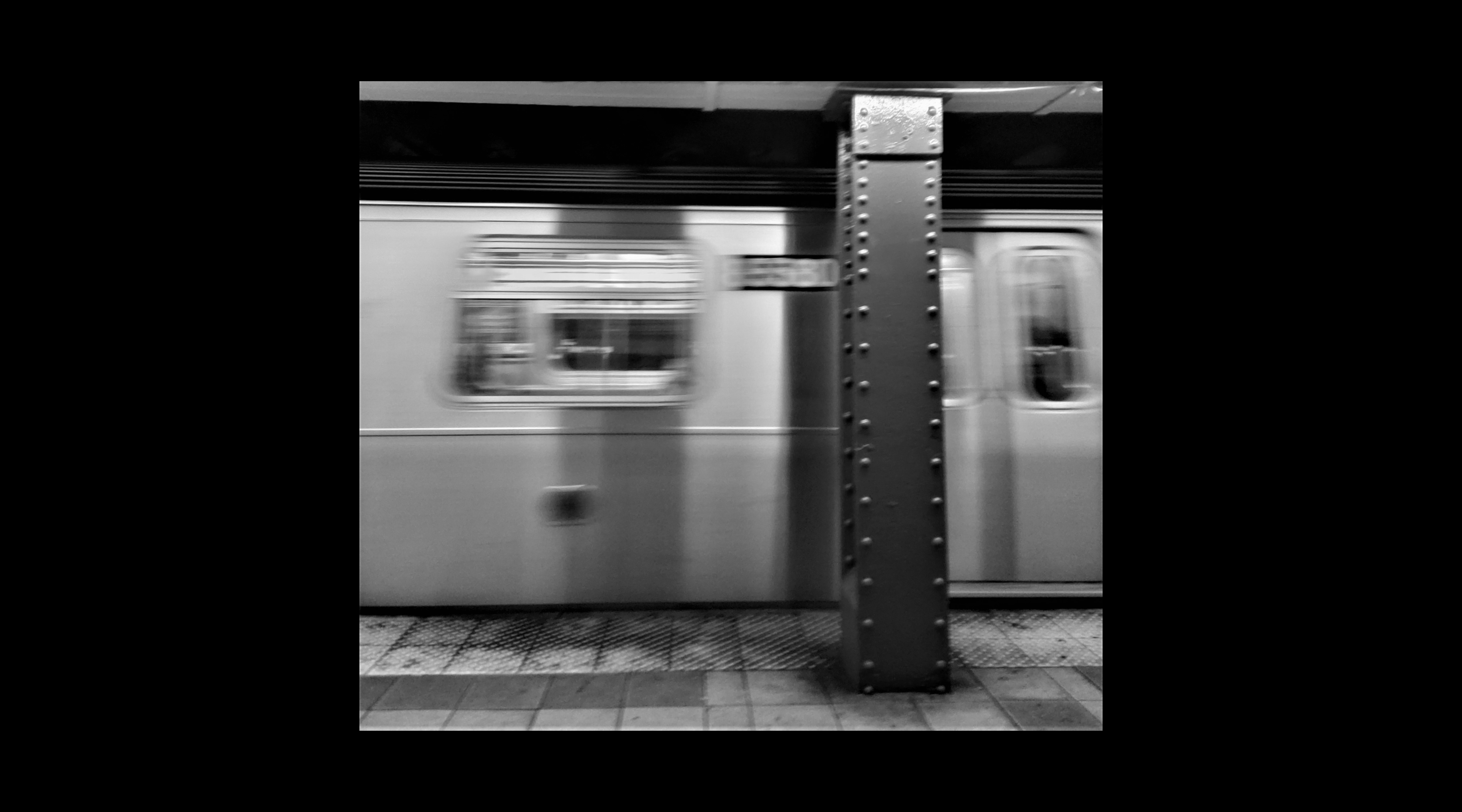 A subway platform, with a moving train (in black and white)