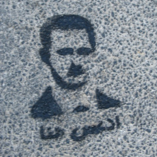 Painted image of Bashar al-Assad with the label “Step Here” on asphalt.