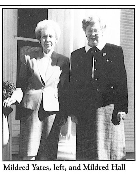 A black and white photo of two eighty-year-old women, both with short hair and wearing blazers and knee-length skirts. 