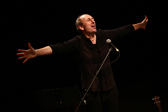 David Cale on stage, arms outspread singing into a microphone. 