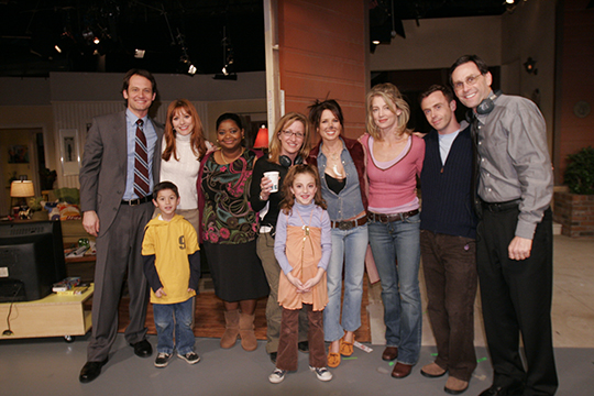 A group photo of ten cast members posed on set