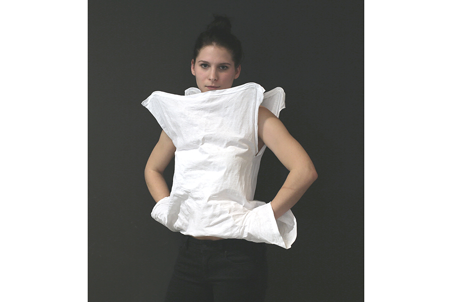 A front view of the stiffened t-shirt, the model's hands tucked into the opening made by the the squared-off base. 