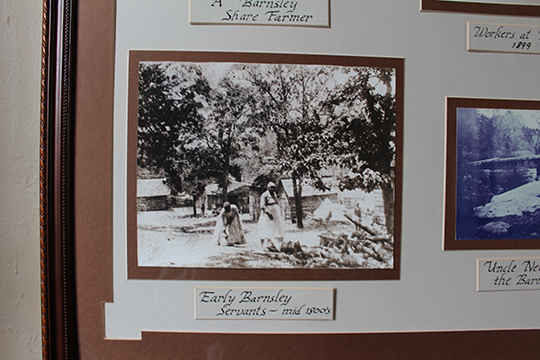 Detail from a scrapbook-style photo display showing a black-and-white photo of two black women in white dresses under a tree outside wood cabins with the caption "Early Barnsley Servants, mid 1800s"