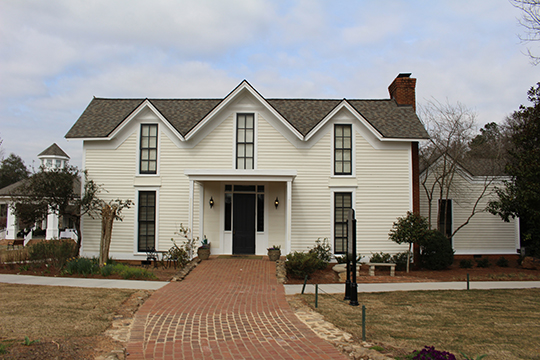 a two-story white building with three peaked eaves and a red brick chimney and the brick path that leads to its entrance