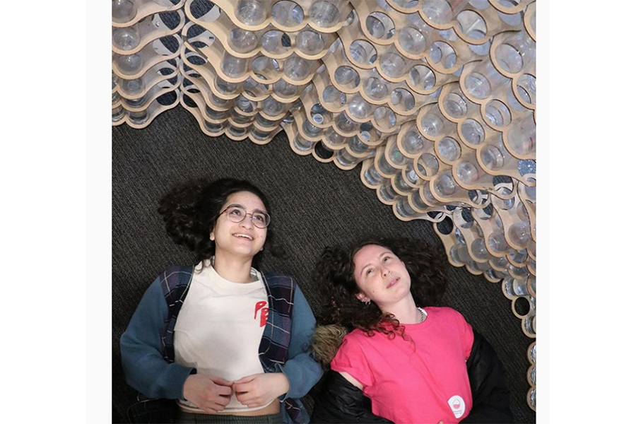 Photograph of two students lying on the floor, looking up at the walls of the "Bottleneck" structure
