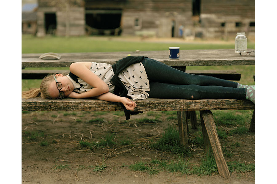 Girl laying down on the seat of a wooden picnic table. 