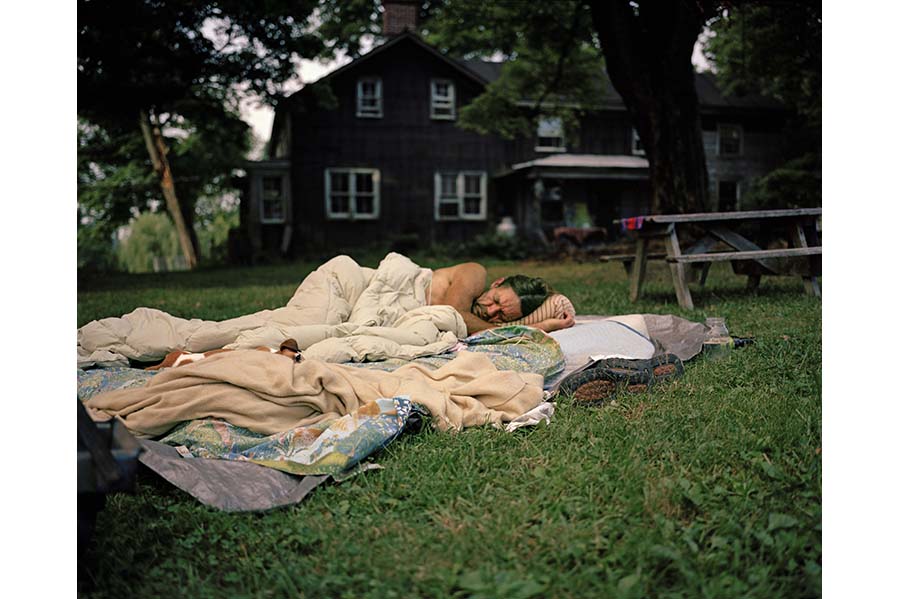 Man lying on blankets on the grass in front of a house. 