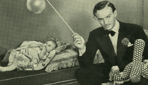 Man in a suit offhandedly entertaining a baby with a mobile.