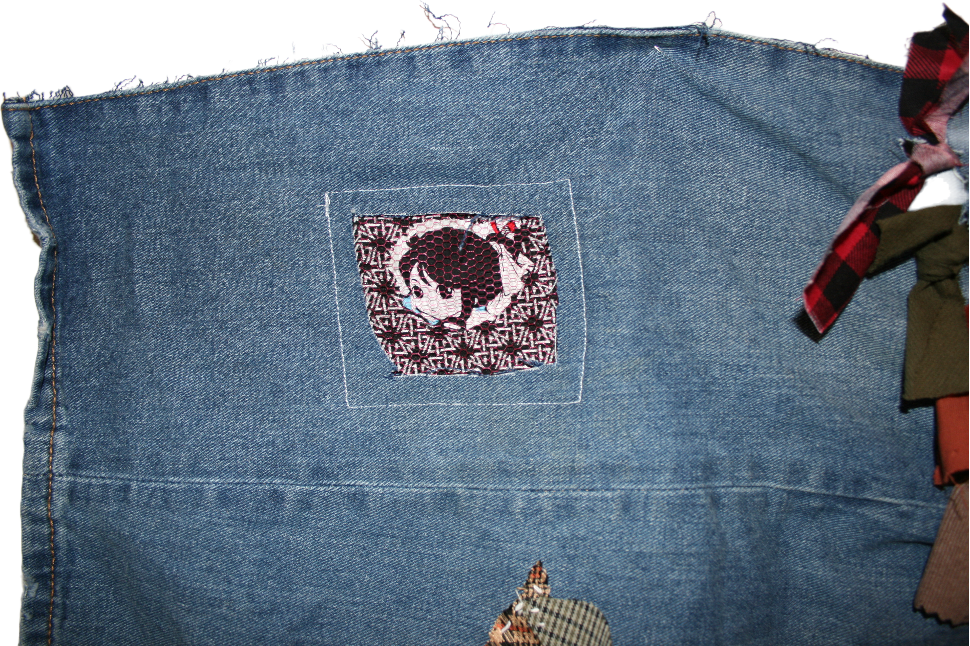 Close up photo of the upper left corner of the piece. There’s a cutout in the denim showing the face of a woman sewn onto black and white patterned fabric and covered by pink mesh.
