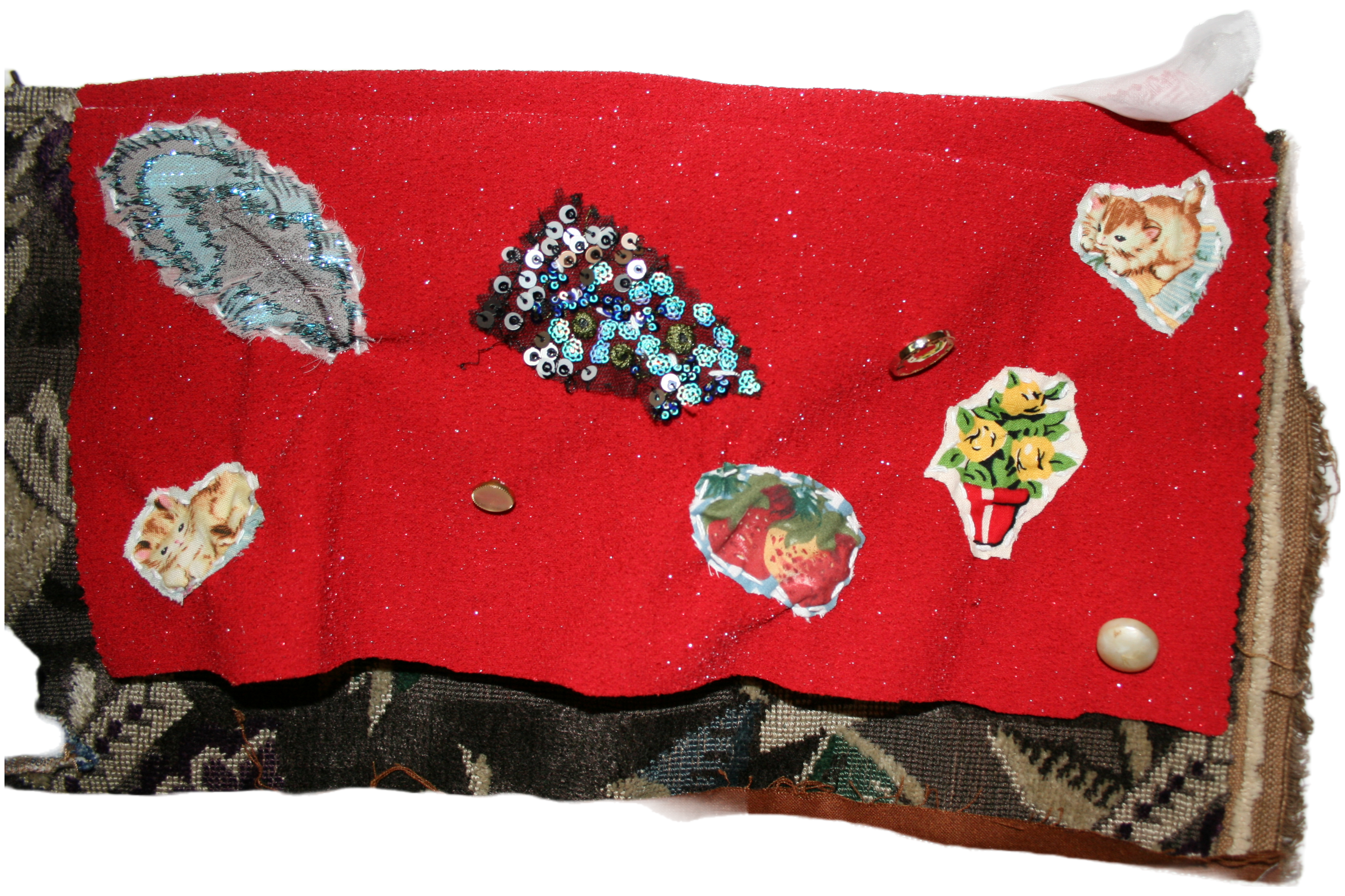Close up photo of the upper right corner of the piece. There is a piece of red fabric with three buttons sewn on it, a feather in the left corner, two cats on the left and right side, some strawberries in the middle, a pot of flowers next to it, and some sequins on the upper side.
