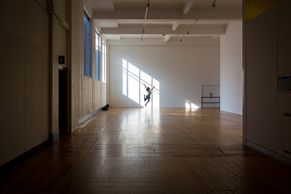 A large empty dance room corridor, with a dancer captured in mid-leap near the back wall. 