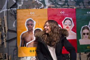 A young woman poses against an ad campaign plastered on a wall. 