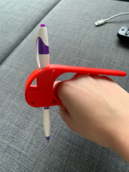 A hand holding a red plastic U-shaped writing tool with a pen perpendicular to the handle.